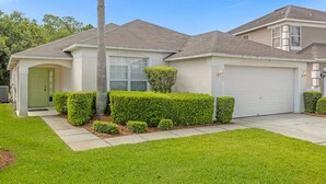 A single-story house with a garage, a front door, and a small front yard with trimmed bushes. - 1061 Lake Berkley 4 Bed with Pool (kissimmee)
