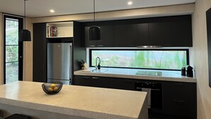 A modern kitchen with dark cabinetry, a stainless steel refrigerator, a large window, and pendant lighting.