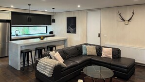 A modern kitchen with a built-in island, a black leather sofa, and a glass coffee table.