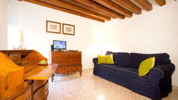 A living room with a wooden coffee table, a blue sofa with green cushions, a wooden chest of drawers, and a television on a wooden cabinet.