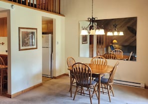 A dining area with a wooden table and chairs, a refrigerator, a framed picture, and a large mirror on the wall.