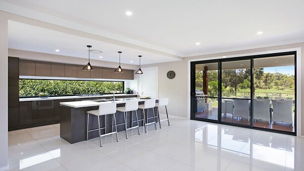 A modern kitchen with a central island, bar stools, and a large sliding glass door leading to an outdoor patio. - Best Cellar - The VIntage Holiday Houses (POKOLBIN)