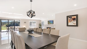 A modern dining room with a large table, chairs, a geometric pendant light, a fireplace, and a TV on the wall. - Best Cellar - The VIntage Holiday Houses (POKOLBIN)