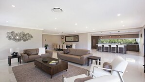 A modern living room with a sofa, coffee table, and chairs, a dining area with a table and chairs, and a kitchen with bar stools. - Best Cellar - The VIntage Holiday Houses (POKOLBIN)