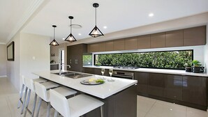 A modern kitchen with a central island, pendant lights, and a view of greenery through a window. - Best Cellar - The VIntage Holiday Houses (POKOLBIN)