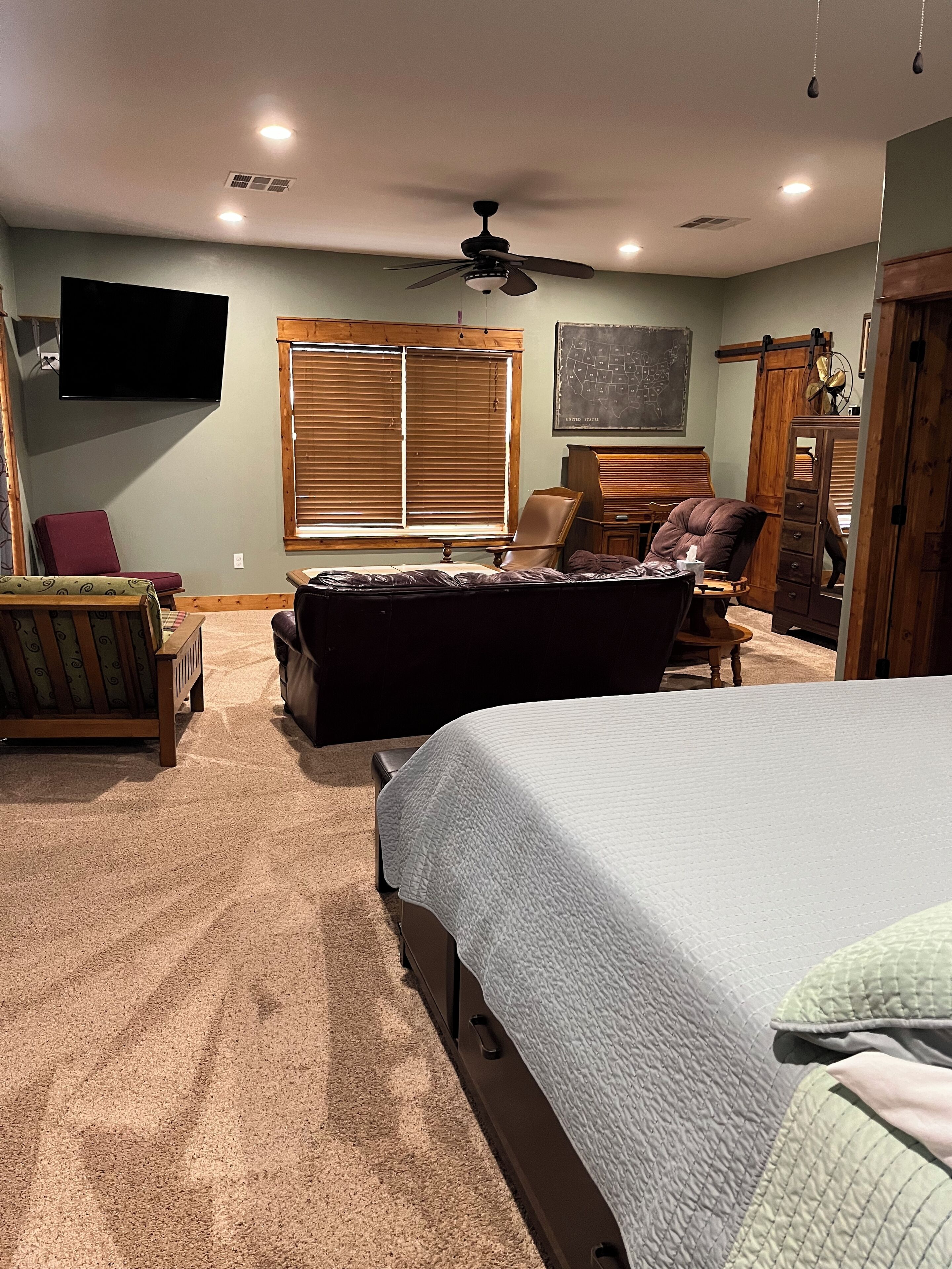 Ein Schlafzimmer mit einem Bett, einem Sessel, einer Couch, einem Fernseher und einem Deckenventilator.