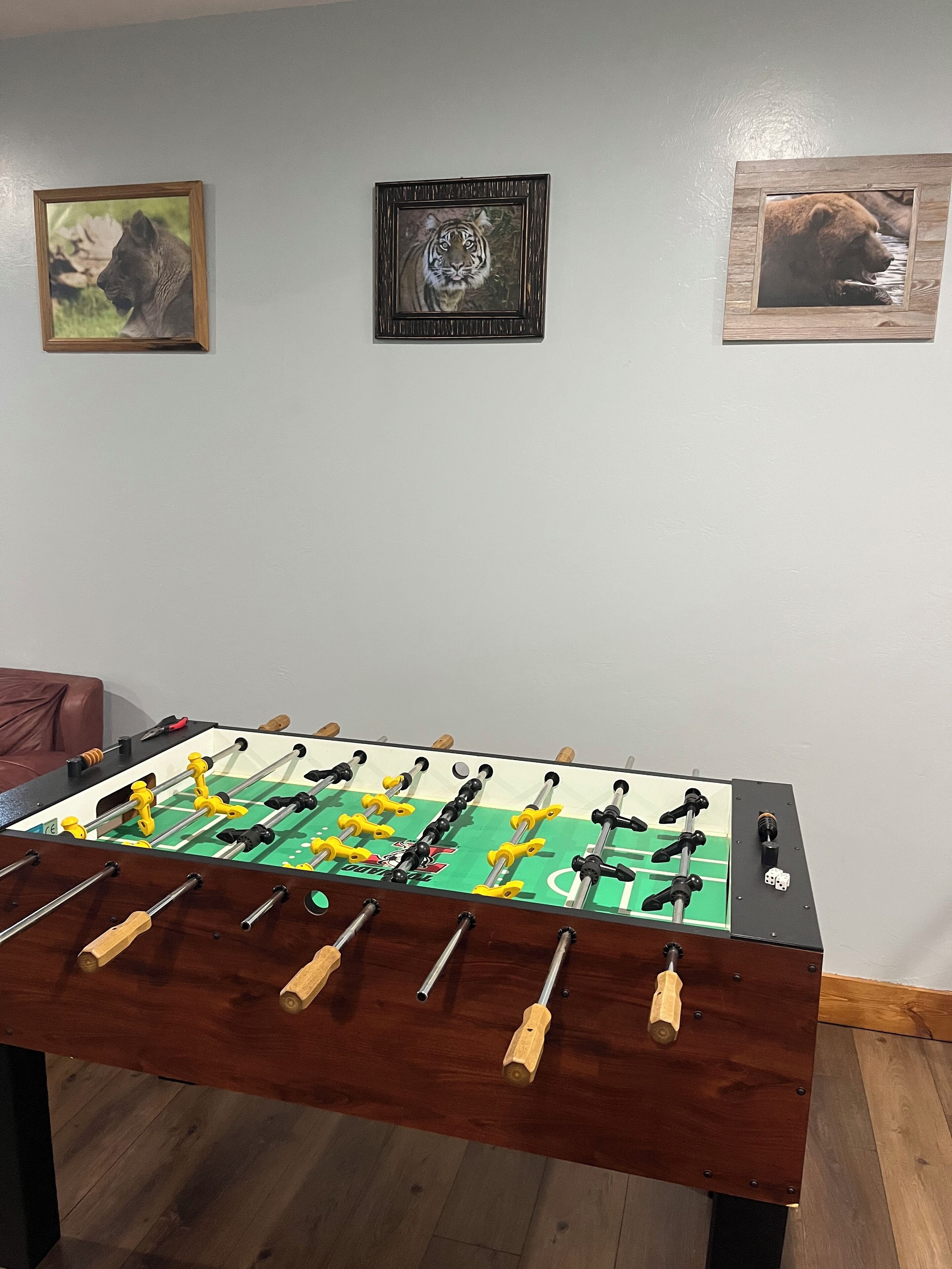 A foosball table in a room with a brown leather couch and three framed animal pictures on the wall.
