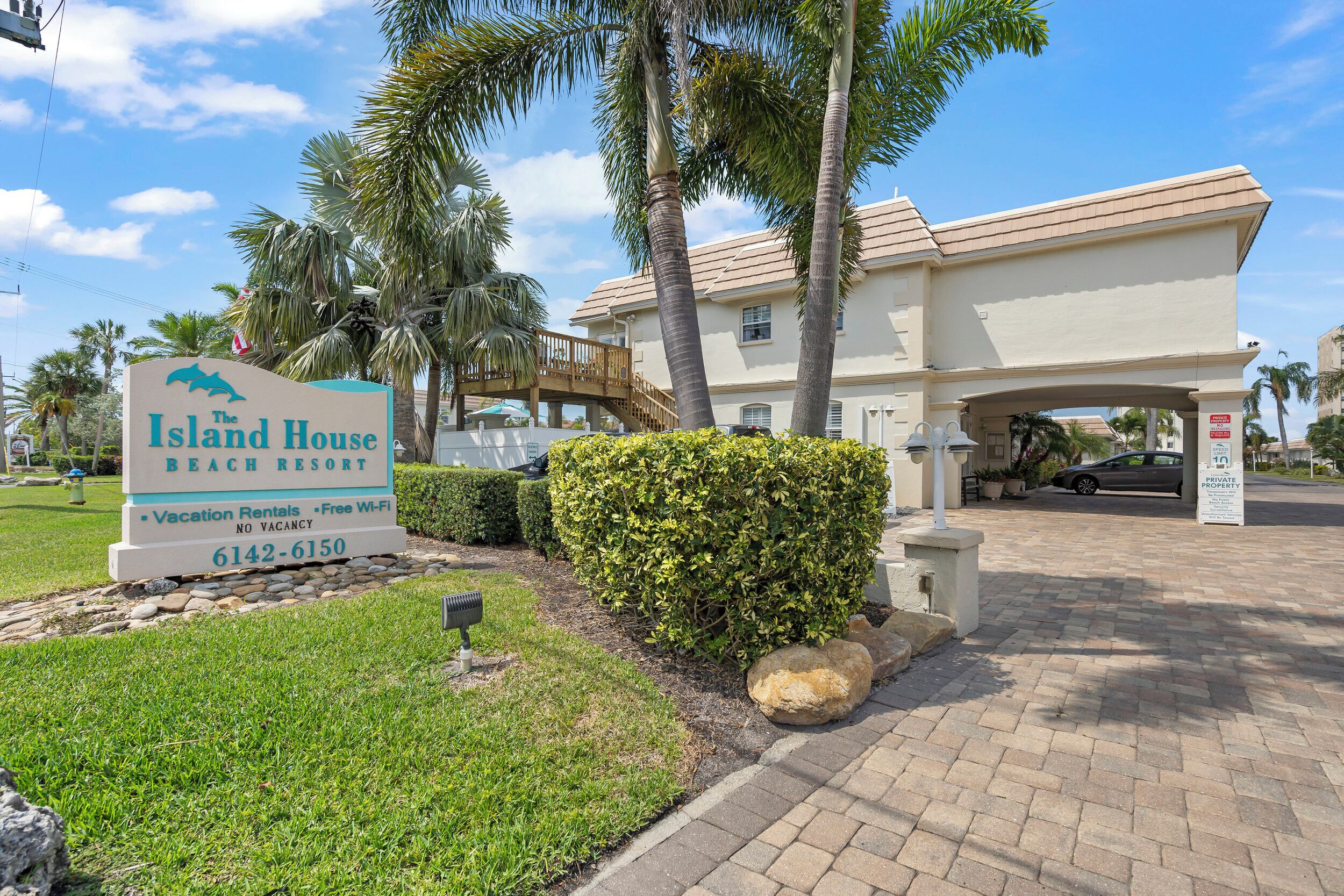 A sign for The Island House Beach Resort with a contact number.