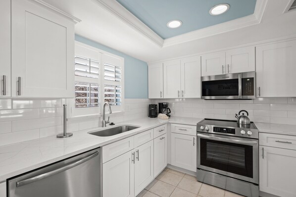 A modern kitchen with white cabinets, stainless steel appliances, and a blue accent wall. - Island House Beach Resort Villa 39 (Siesta Key)