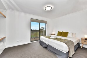 Ein Schlafzimmer mit Bett, Nachttisch, Lampe, Fenster mit Blick ins Freie und Deckenleuchte.