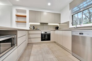 A modern kitchen with built-in appliances, a dishwasher, and a window with a view of trees.