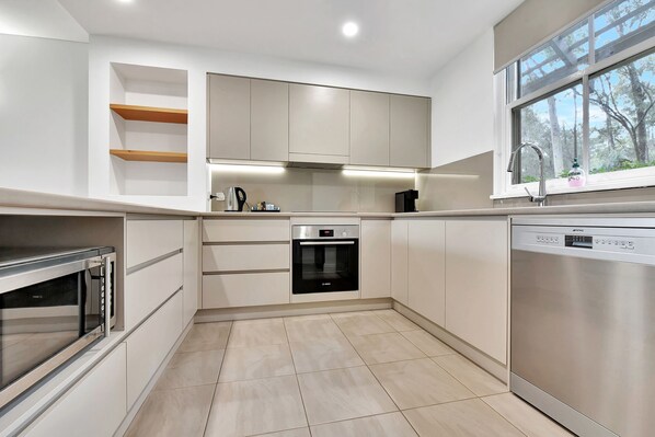 A modern kitchen with built-in appliances, a dishwasher, and a window with a view of trees.