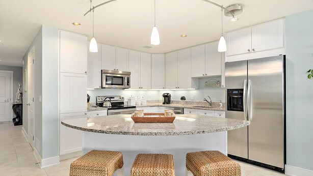 A modern kitchen with white cabinets, stainless steel appliances, a granite countertop, and three woven stools.