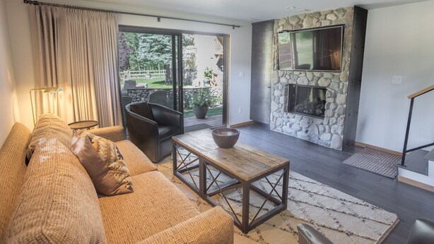 A modern living room with a stone fireplace, a sofa, a coffee table, and a view of the outdoors. - Great 2 bed townhouse. This is the best location in Ketchum! (Ketchum)