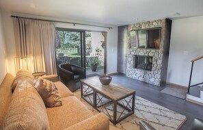 A modern living room with a stone fireplace, a sofa, a coffee table, and a view of the outdoors.