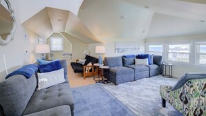 A spacious living room with a high ceiling, grey sofas, a patterned armchair, and a view through large windows. - Nantucket Charm | 280 ft from the Beach | Private Pool (Virginia Beach)