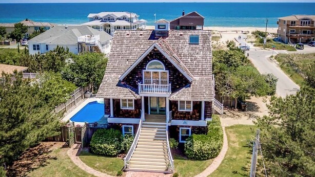 A large two-story house with a prominent front entrance, a balcony, and a swimming pool. - Nantucket Charm | 280 ft from the Beach | Private Pool (Virginia Beach)