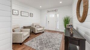 Ett rum med två beige fåtöljer, ett mörkt träbord, en grå, mönstrad matta och en skylt ovanför dörren med texten "BEACH HOUSE".