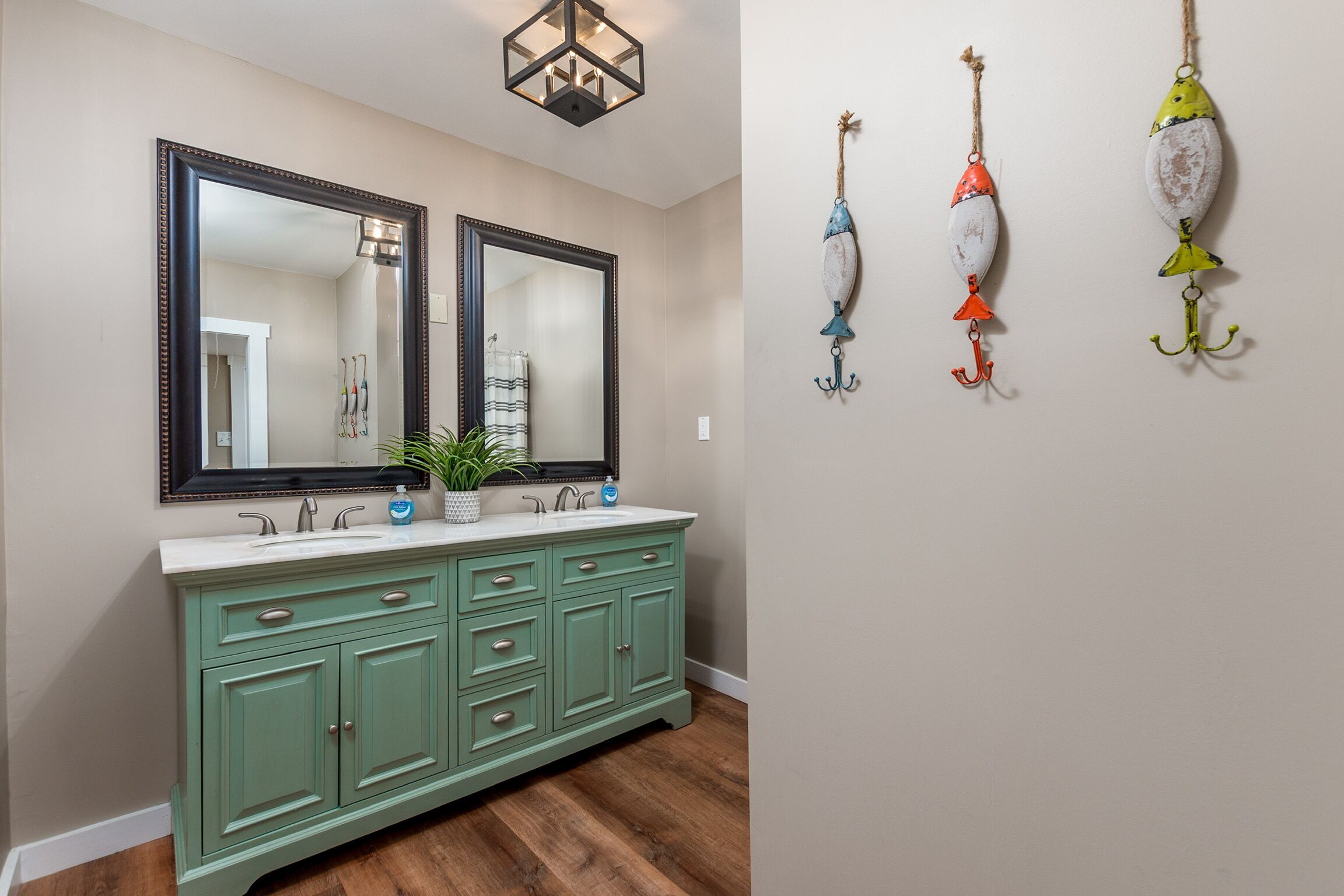 Une salle de bain avec un meuble-lavabo vert, deux miroirs et trois leurres de pêche accrochés au mur.