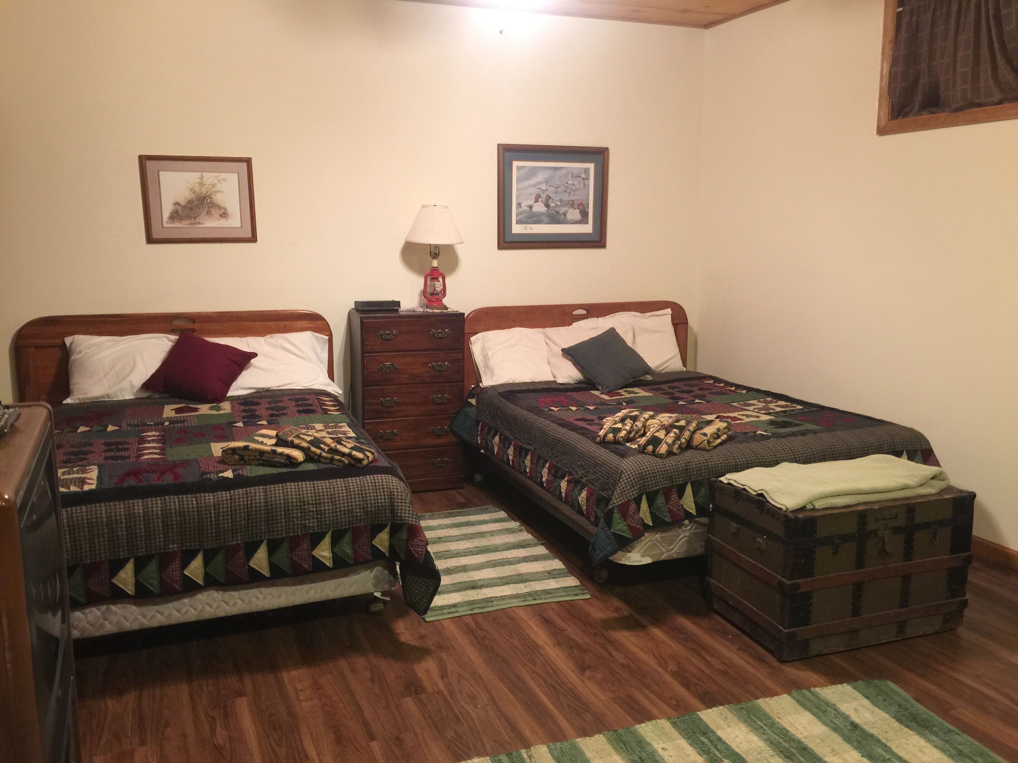 Une chambre avec deux lits simples, une commode, une lampe et une petite commode à tiroirs.