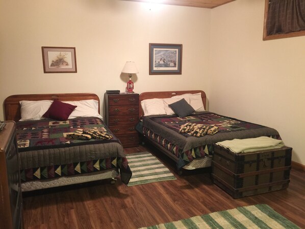 Une chambre avec deux lits simples, une commode, une lampe et une petite commode à tiroirs.
