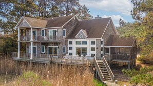 A two-story house with a deck and stairs leading to a covered porch. - Castlebar | Luxury Salt Marsh Landing Waterfront w/ Private Pier, Bayfront Dock, Sunsets & Fireplace (Chincoteague Island)