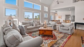 A spacious living room with a large window, a ceiling fan, and a wooden coffee table. - Castlebar | Luxury Salt Marsh Landing Waterfront w/ Private Pier, Bayfront Dock, Sunsets & Fireplace (Chincoteague Island)