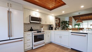 Une cuisine moderne avec des meubles blancs, des appareils en acier inoxydable et un plafond en bois.