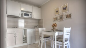A modern kitchen with white cabinetry, a microwave, and a dining area with two chairs and a table.