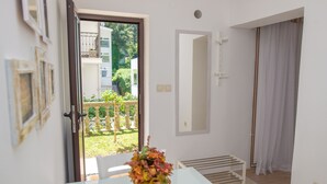 A room with a white table, a vase with flowers, a door leading to an outdoor area, and a white bench.