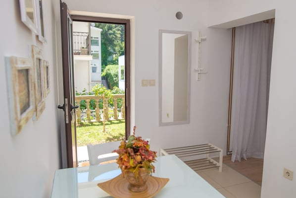 A room with a white table, a vase with flowers, a door leading to an outdoor area, and a white bench.