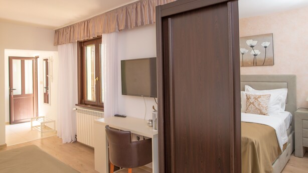 A bedroom with a bed, a desk, a chair, a TV, and a painting on the wall.