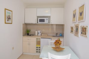 A compact kitchen with white cabinets, a microwave, a sink, and a dining area with a table and chairs.