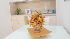 A kitchen with white cabinets, a microwave, a sink, and a decorative vase with autumn leaves on a white table.