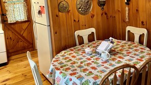 A wooden-paneled dining room with a table set for four, a hanging lamp, and a refrigerator. - A beautiful lake view cabin on Friends Lake   (Chestertown)