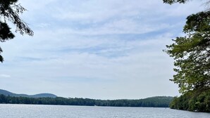 A sandy beach with boats docked at a pier, a clear sky, and a forested hill in the background. - A beautiful lake view cabin on Friends Lake   (Chestertown)