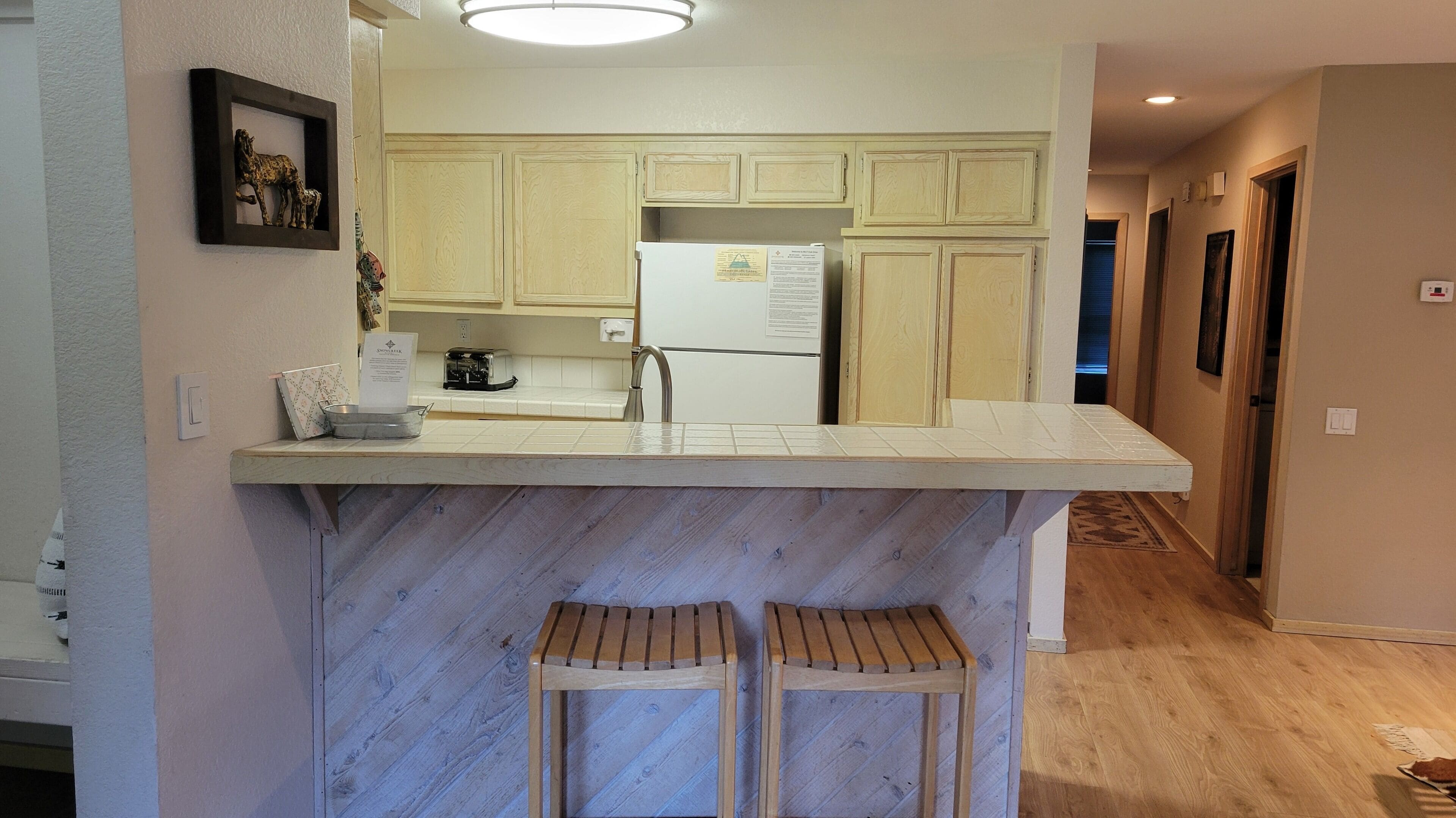 A kitchen with a marble island, wooden stools, a refrigerator, and wooden cabinets.