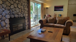 A living room with a stone fireplace, a leather sofa, a wooden coffee table, and a bookshelf. - Snowcreek Resort Vacation Rental 617 (Mammoth Lakes)