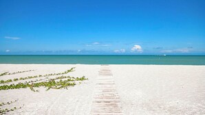 A sandy beach with a wooden walkway leading to the water, clear skies, and a distant boat. - New Latitude Beachfront Captiva Luxury Estate (Captiva)