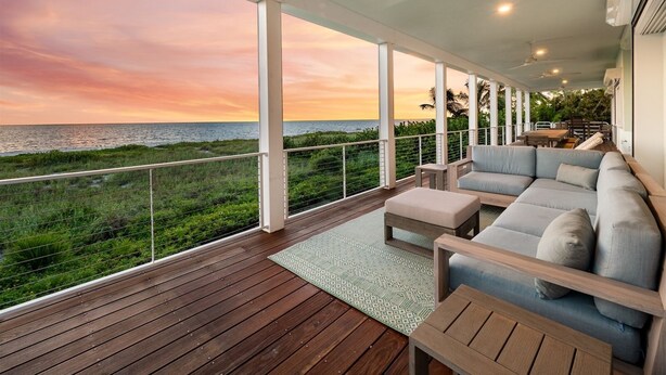 A spacious balcony with a wooden deck, a grey sofa, and a table. - New Latitude Beachfront Captiva Luxury Estate (Captiva)