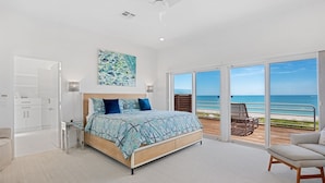 A bedroom with a large bed, a ceiling fan, a view of the ocean through sliding glass doors, and a beach chair on the balcony. - New Latitude Beachfront Captiva Luxury Estate (Captiva)