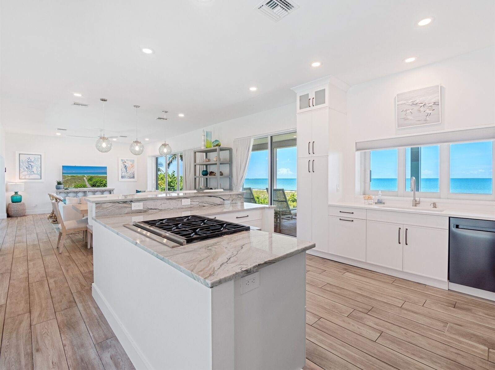 Una cocina moderna con una isla grande, armarios blancos y vista al océano.