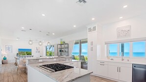 A modern kitchen with a large island, white cabinetry, and a view of the ocean. - New Latitude Beachfront Captiva Luxury Estate (Captiva)