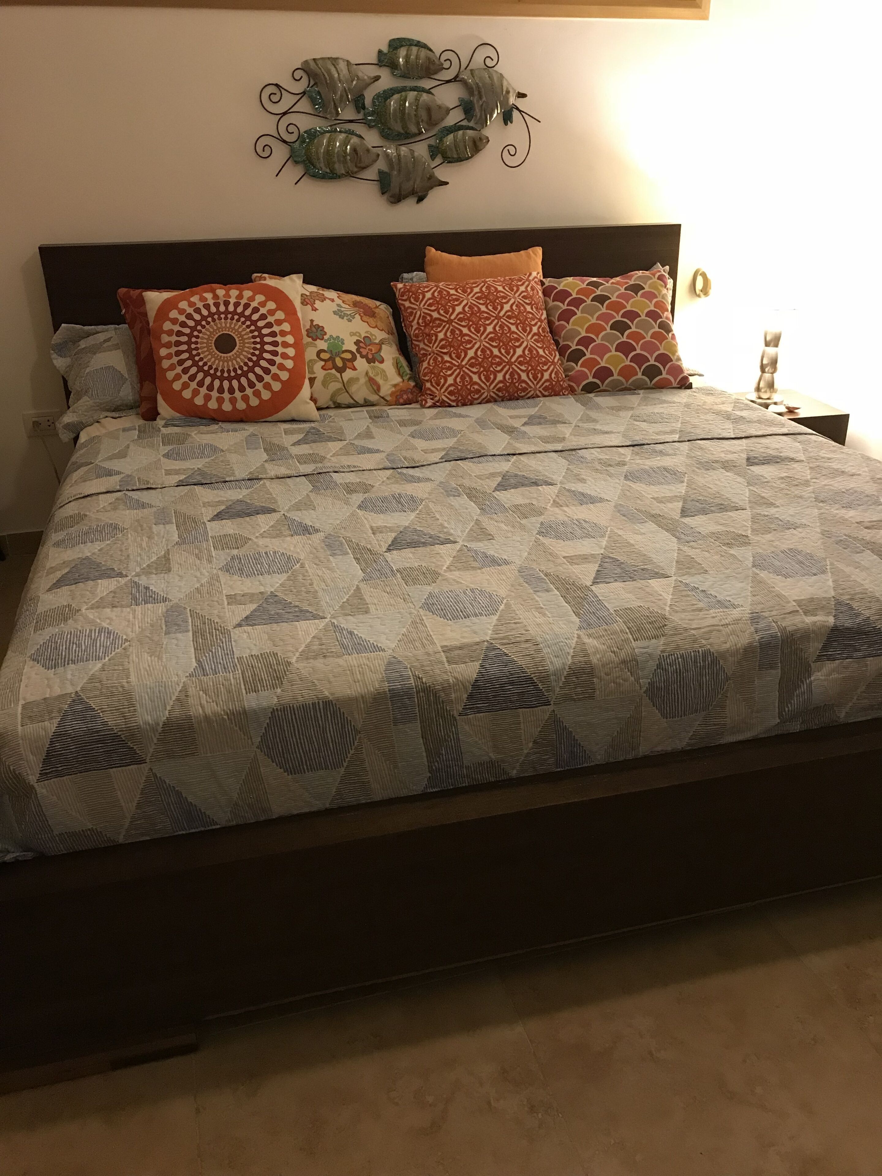 A bed with a patterned quilt, multiple pillows, and a wall decoration above.