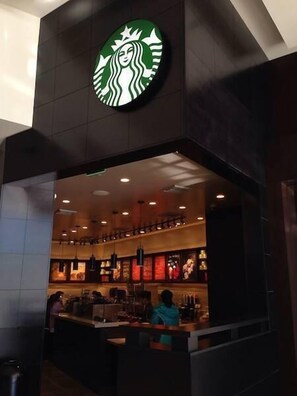 Una tienda Starbucks con fachada oscura y un interior visible que muestra una barra de servicio y zona de estar.