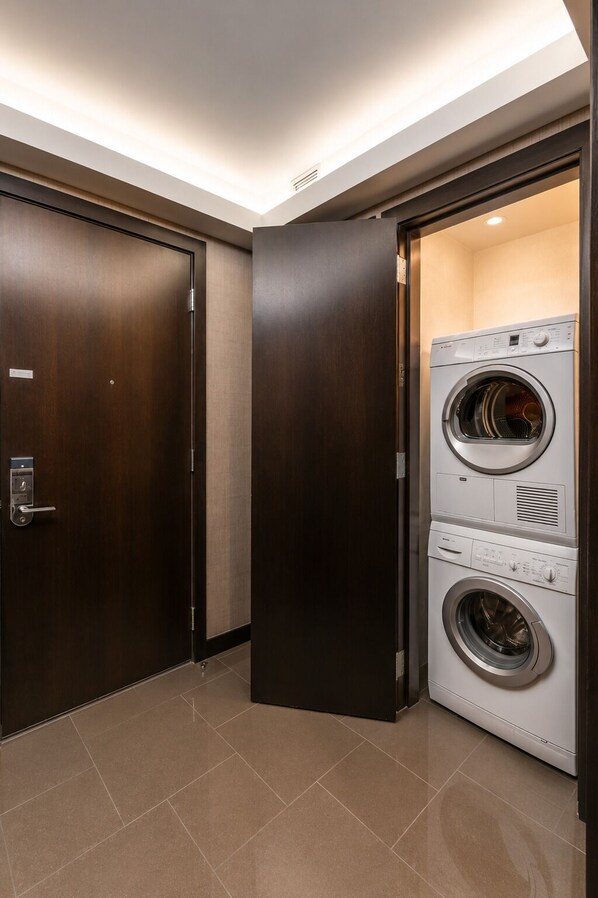 A hotel room with a dark wooden door, a washing machine, and a tiled floor.