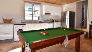 A compact kitchen with a pool table, white cabinets, and a stainless steel refrigerator. - Enjoy the waterfront and outdoor activities while staying at our place! (Lota)