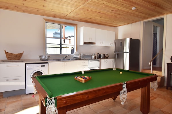 A compact kitchen with a pool table, white cabinets, and a stainless steel refrigerator.