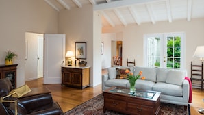 Un salon spacieux avec un plafond haut, un canapé gris, une table basse en bois et un tapis à motifs.