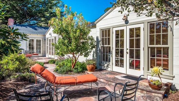Une terrasse avec des meubles d’extérieur, une plante en pot et une maison dotée de grandes fenêtres et d’une porte.